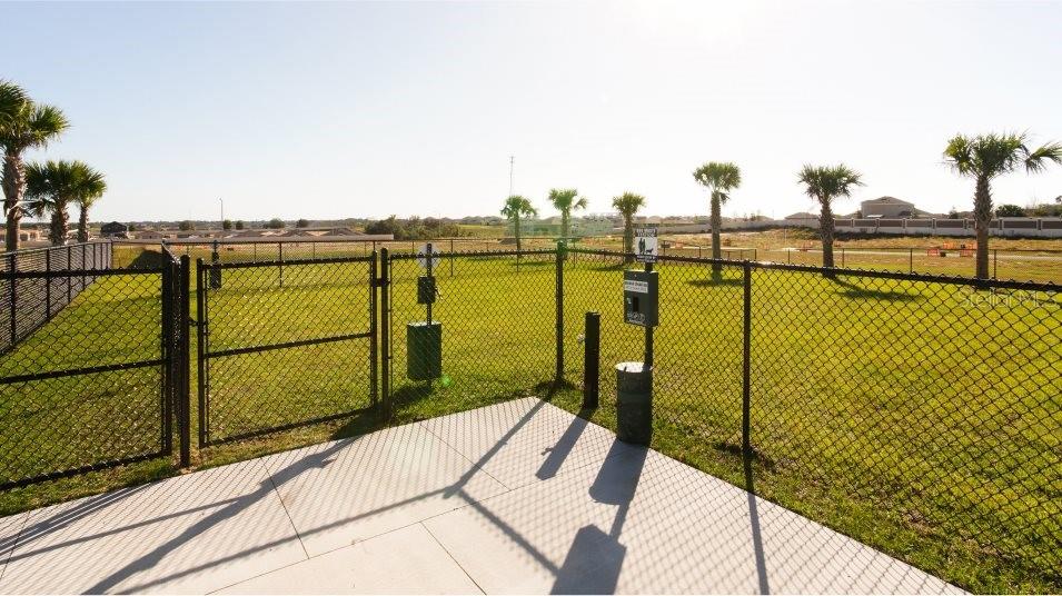 A fenced-in dog park features a concrete patio, a waste station, and several palm trees — 2089 LASSO LOOP, EAGLE LAKE, FL