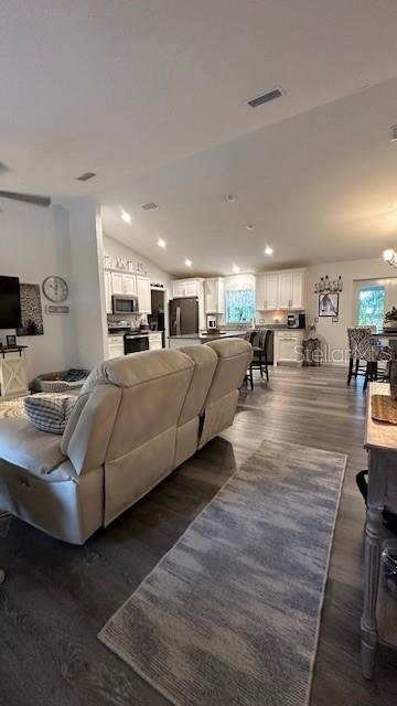 An open-concept living room with a recliner sofa leads into a kitchen with white cabinets — 1113 PORSCHE AVENUE, SEBRING, FL