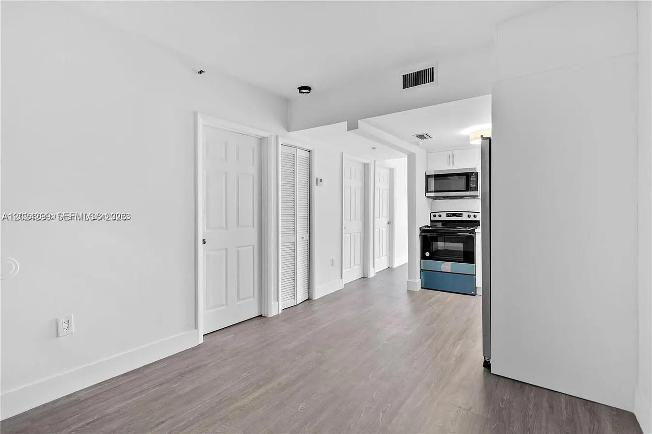 A kitchen with stainless steel appliances and white cabinets opens into a light-floored living area — 1351 SW 4th St # 8, Miami FL 33135, MIAMI, FL