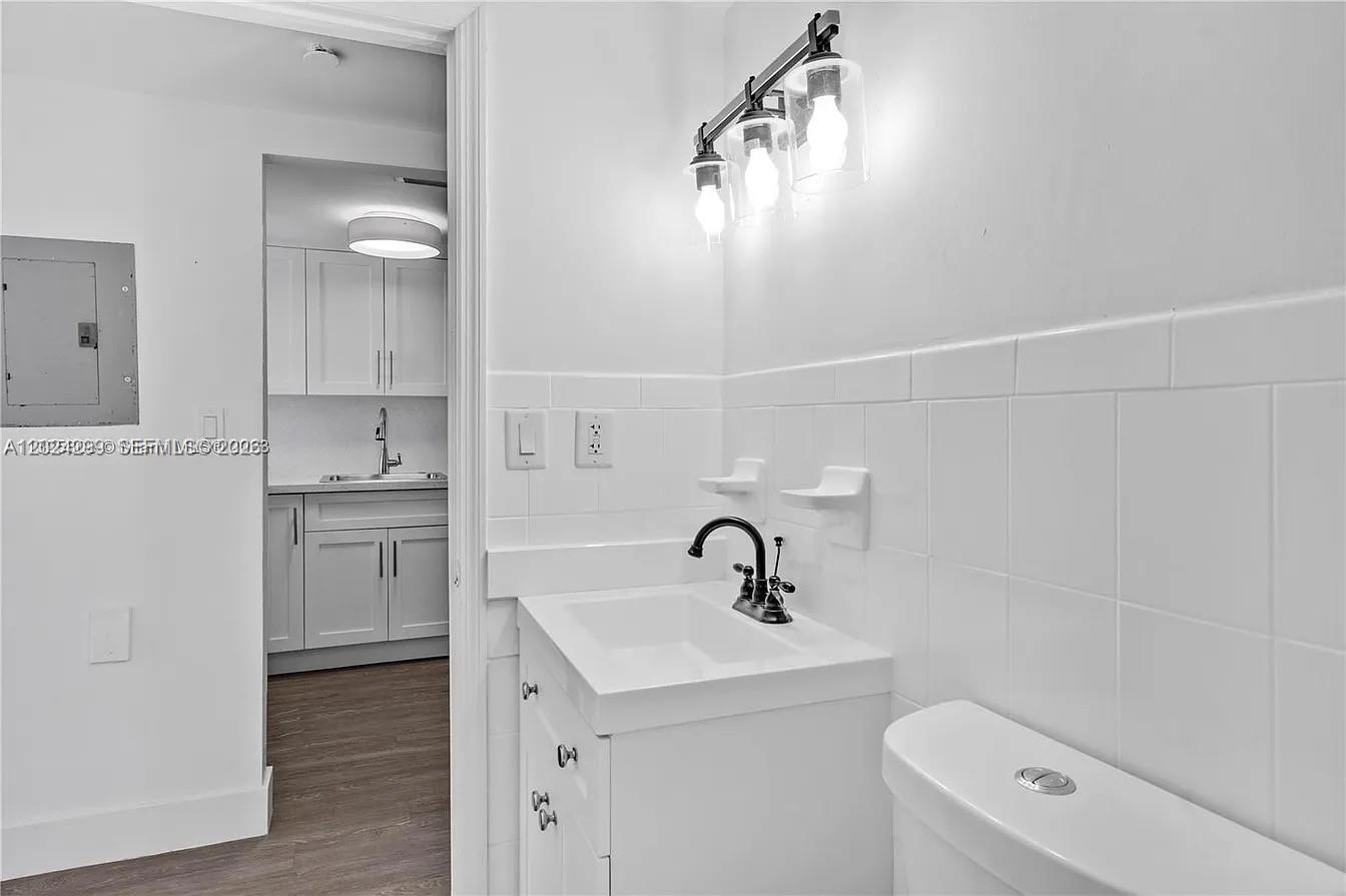 A small bathroom with a white vanity and sink sits adjacent to a kitchen — 1351 SW 4th St # 8, Miami FL 33135, MIAMI, FL