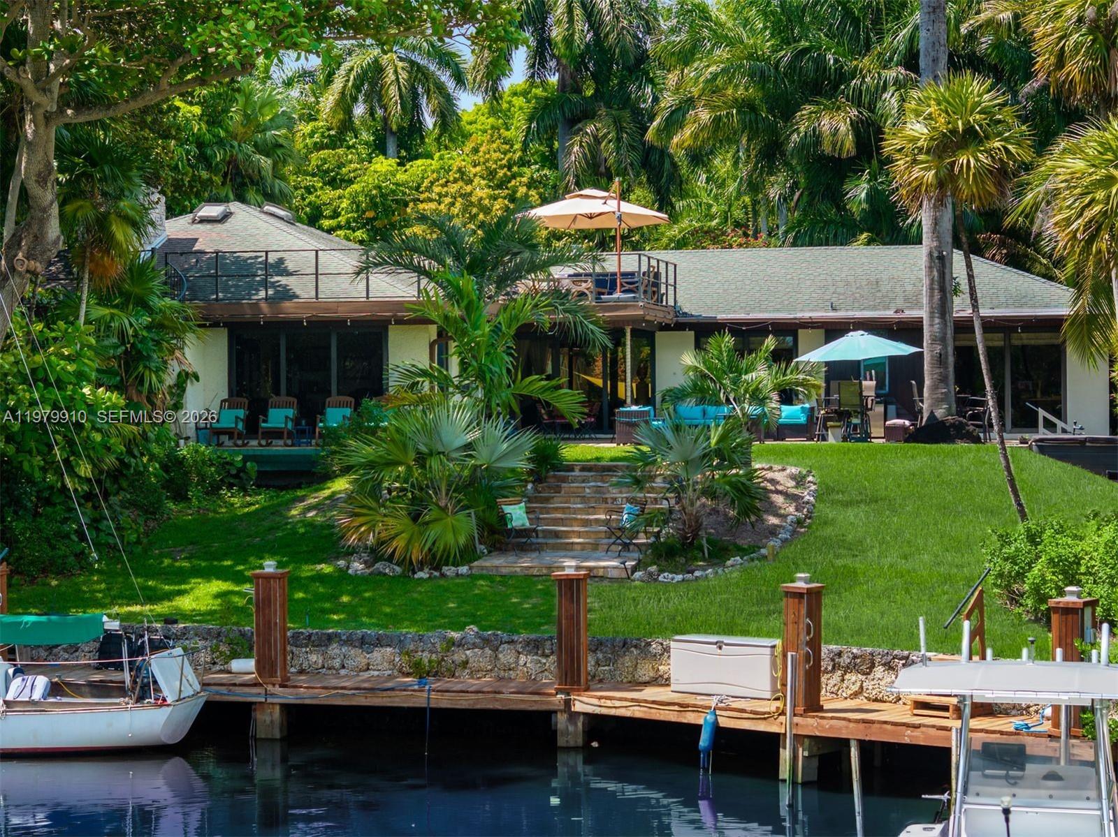 A waterfront house with a wooden dock, green lawn, stone steps, and a rooftop deck — 3373 Poinciana Ave, Miami FL 33133, MIAMI, FL
