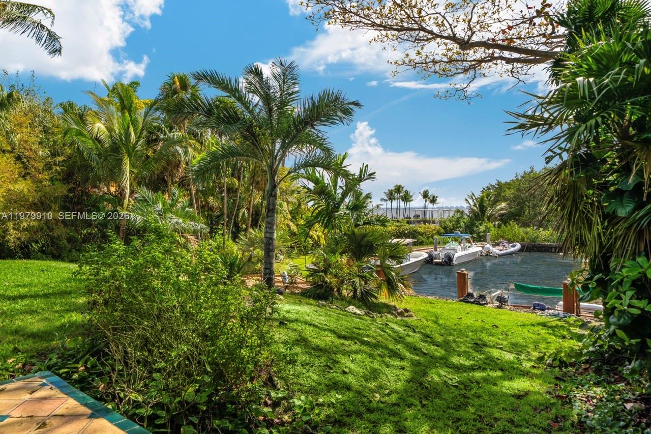 A grassy backyard features palm trees, lush landscaping, and a private boat dock on water — 3373 Poinciana Ave, Miami FL 33133, MIAMI, FL