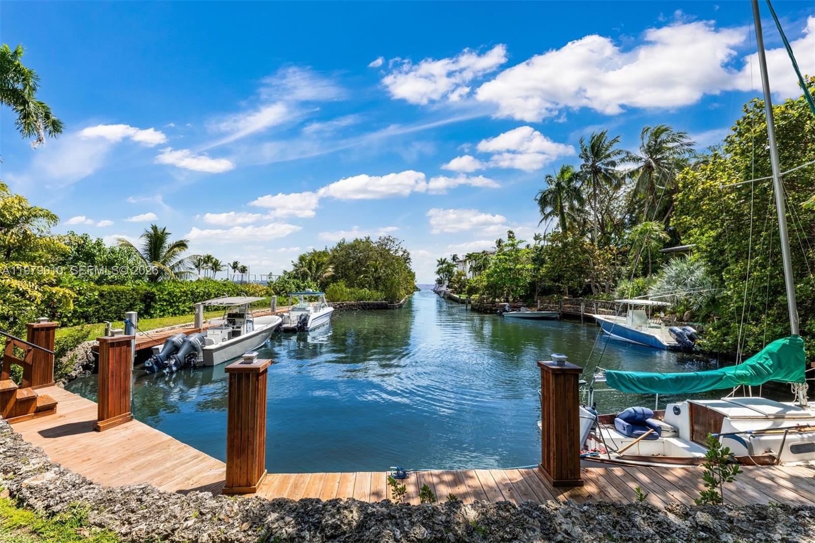 A wooden dock overlooks a narrow canal lined with boats, lush vegetation, and palm trees — 3373 Poinciana Ave, Miami FL 33133, MIAMI, FL