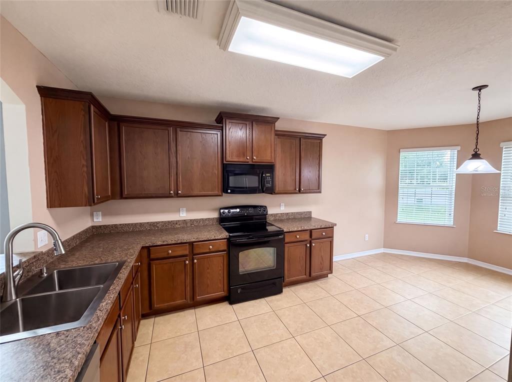 A kitchen features dark wood cabinets, brown laminate countertops, black appliances, and light tile flooring — 12902 SCOUT COURT, GRAND ISLAND, FL