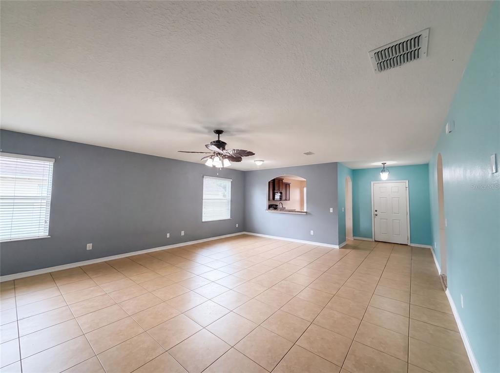 An open-concept living area features light blue walls, beige tile flooring, and a ceiling fan — 12902 SCOUT COURT, GRAND ISLAND, FL