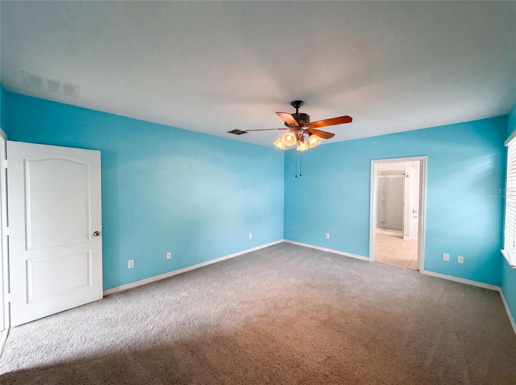 A bedroom with bright blue walls, gray carpeting, a ceiling fan, and an attached bathroom — 12902 SCOUT COURT, GRAND ISLAND, FL