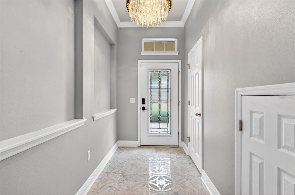 A bright entryway features gray walls, a crystal chandelier, tiled flooring, and a glass-paneled door — 14310 BARRINGTON STOWERS DRIVE, LITHIA, FL