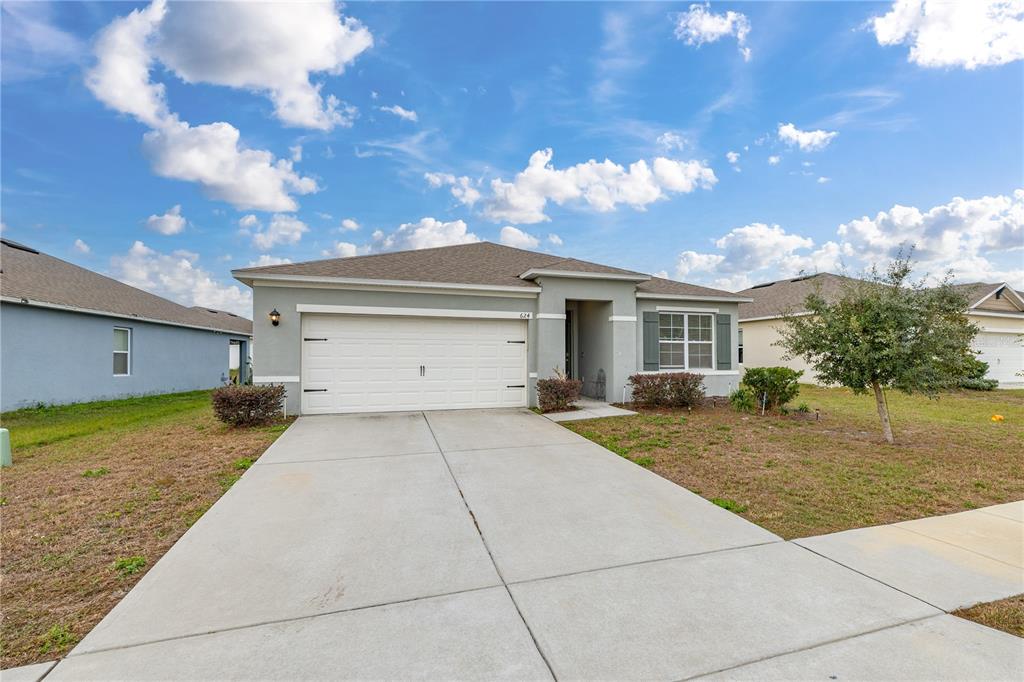 A single-story house with a white garage door, gray stucco exterior, and a concrete driveway — 624 HONEY BELL ROAD, WINTER HAVEN, FL