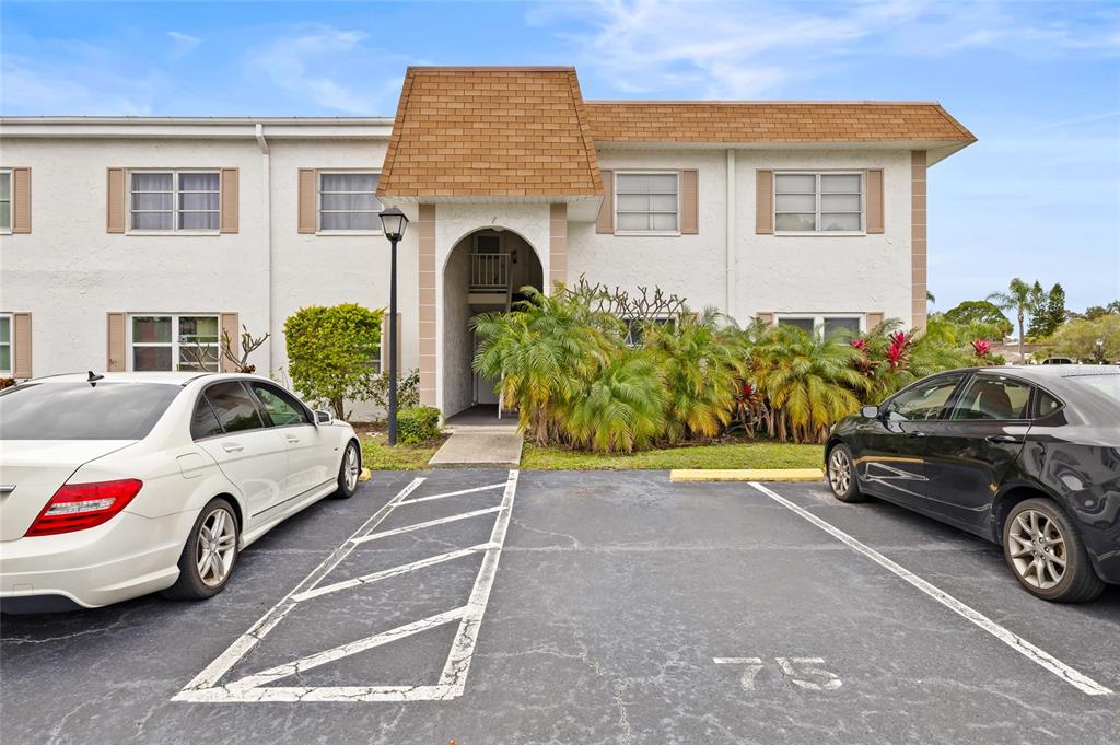 A two-story apartment building exterior features a central arched entryway and two parked cars — 379 S MCMULLEN BOOTH ROAD UNIT 75, CLEARWATER, FL