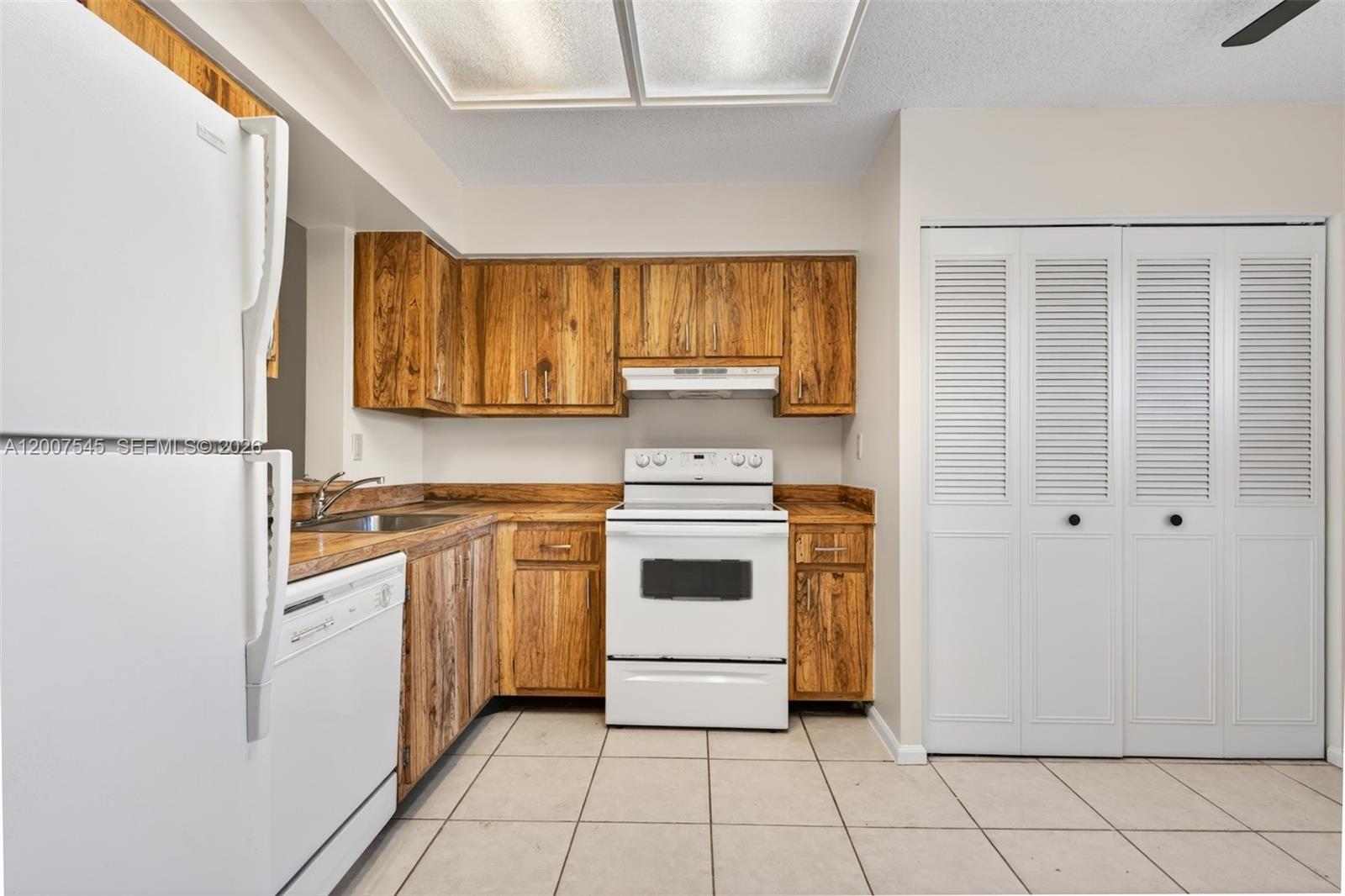 A kitchen features wood cabinets, white appliances, a tiled floor, and a white louvered closet — 357 N Rock Island Rd # 207, Margate FL 33063, MARGATE, FL