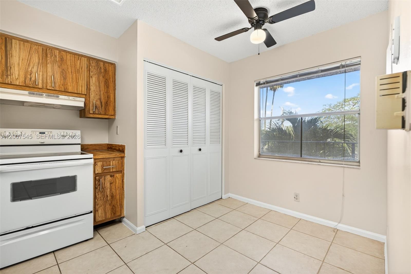 A kitchen features wood cabinets, a white stove, tiled floors, and a louvered closet door — 357 N Rock Island Rd # 207, Margate FL 33063, MARGATE, FL