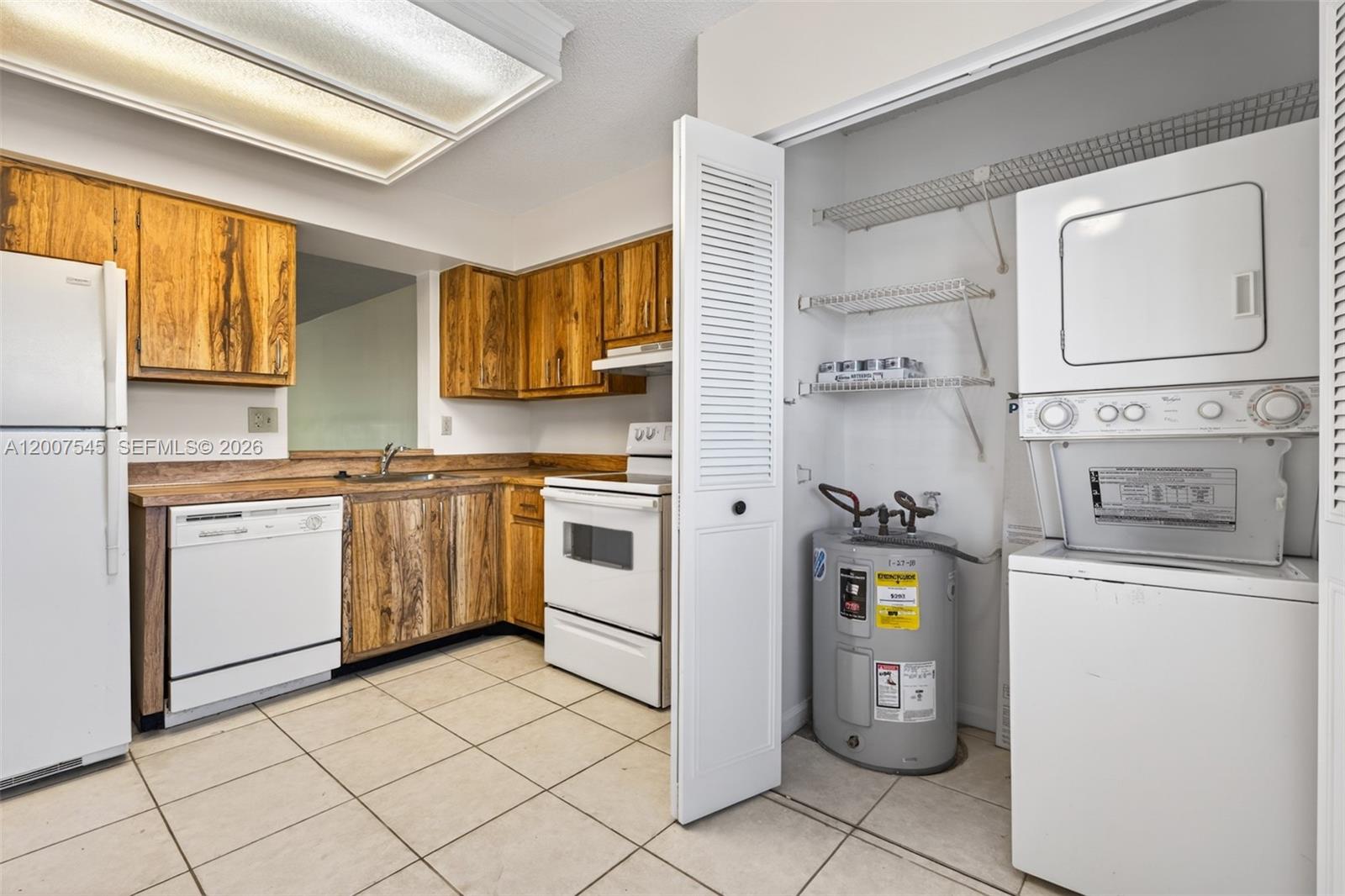 A kitchen with wood cabinets, white appliances, tile flooring, and an adjacent laundry closet — 357 N Rock Island Rd # 207, Margate FL 33063, MARGATE, FL
