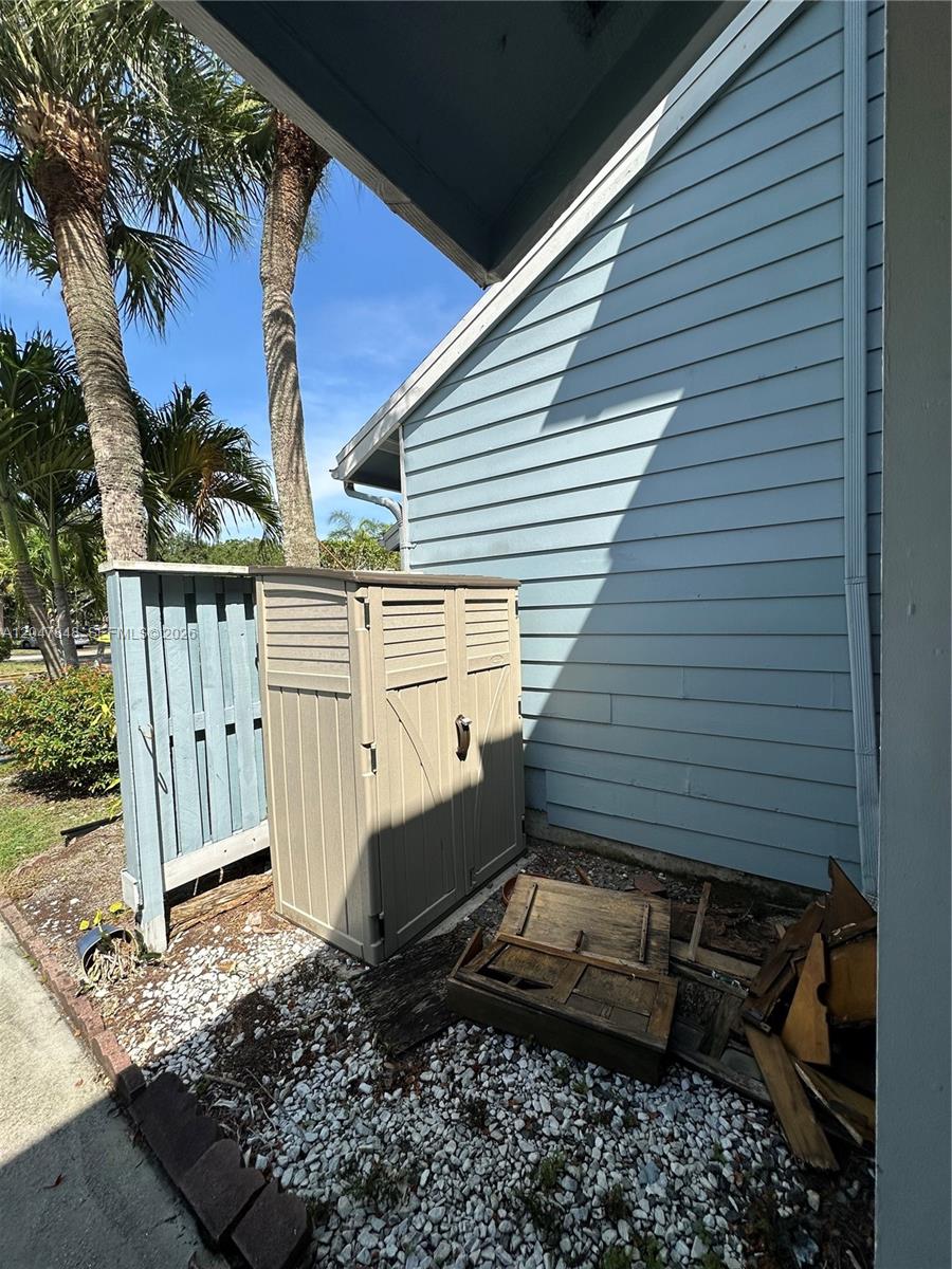 An outdoor storage shed sits next to a blue-sided house wall with debris nearby — 2012 Champions Way, North Lauderdale FL 33068, NORTH LAUDERDALE, FL