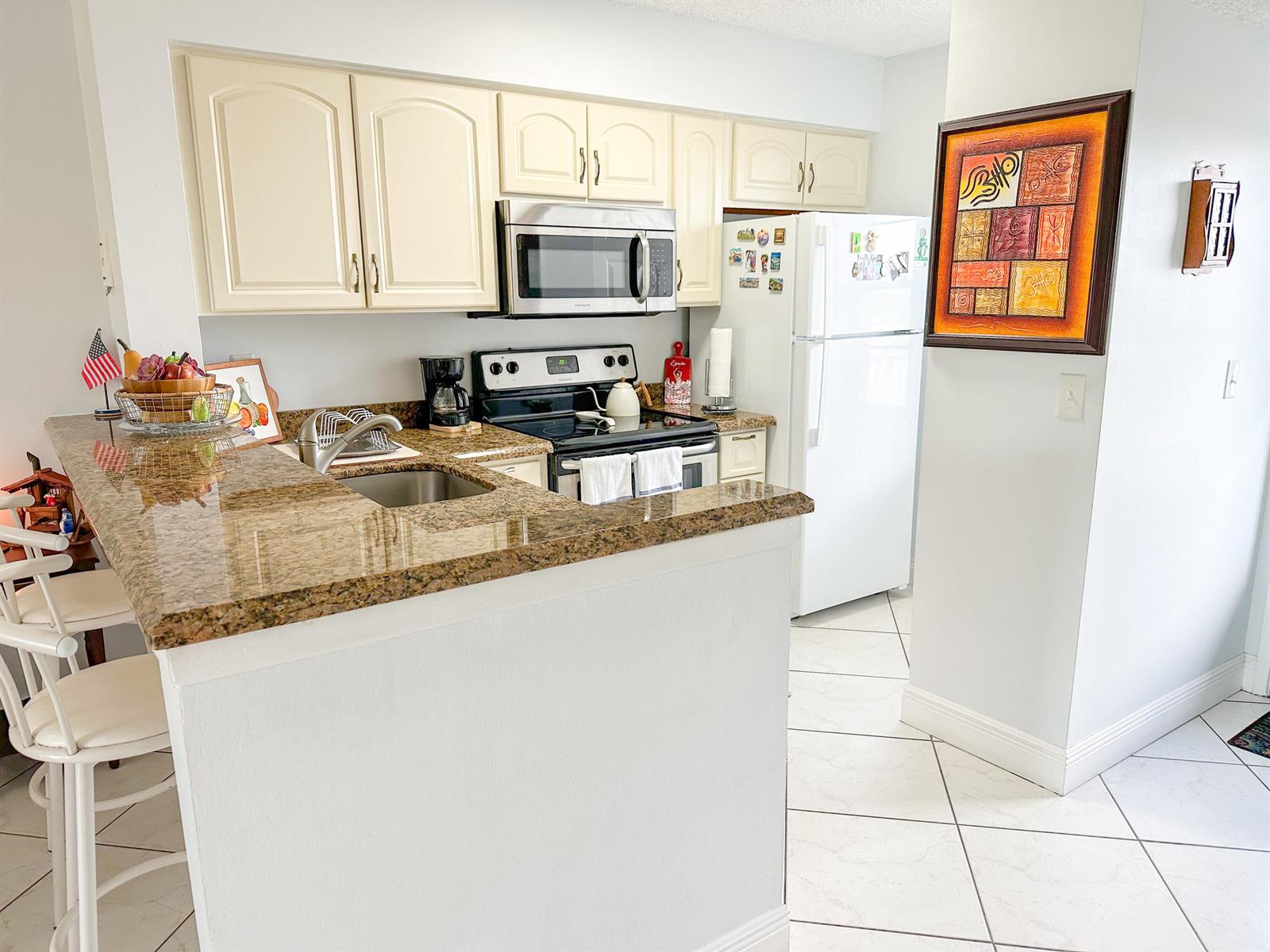 A kitchen features cream cabinets, granite countertops, stainless steel appliances, and white tile flooring — 2222 N Cypress Bend Drive # 403, Pompano Beach FL 33069, POMPANO BEACH, FL