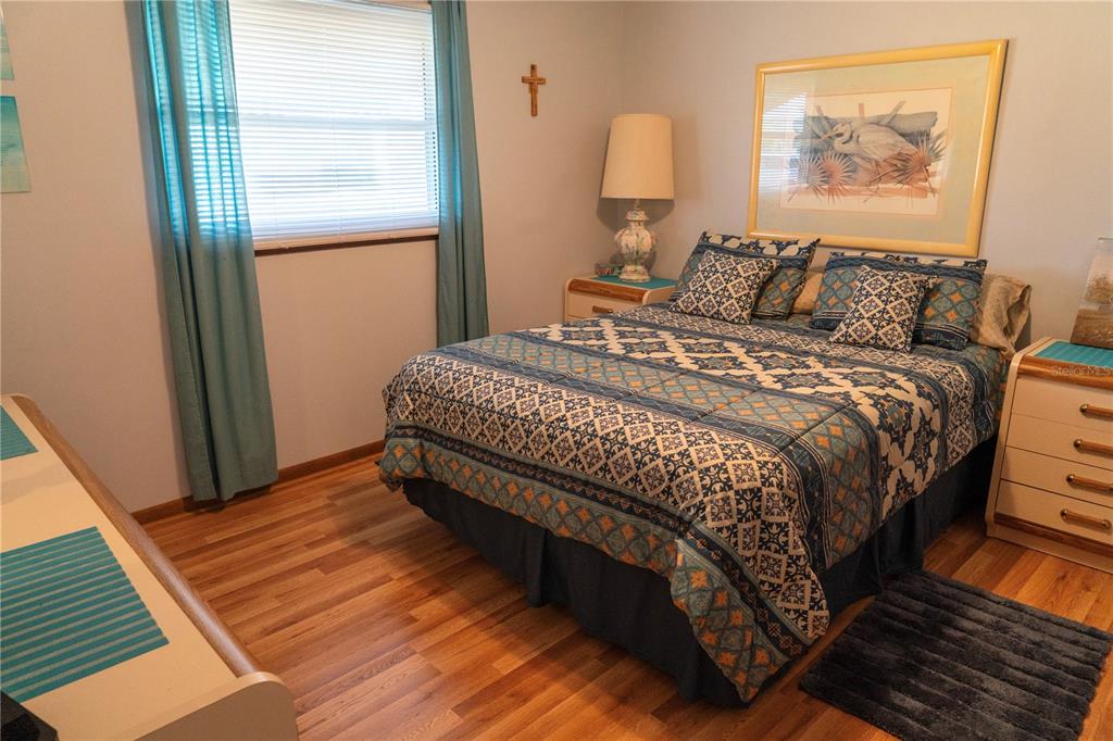 A bedroom features a patterned bedspread, a bedside lamp, a framed print, and wood flooring — 10041 SW 97TH COURT, OCALA, FL