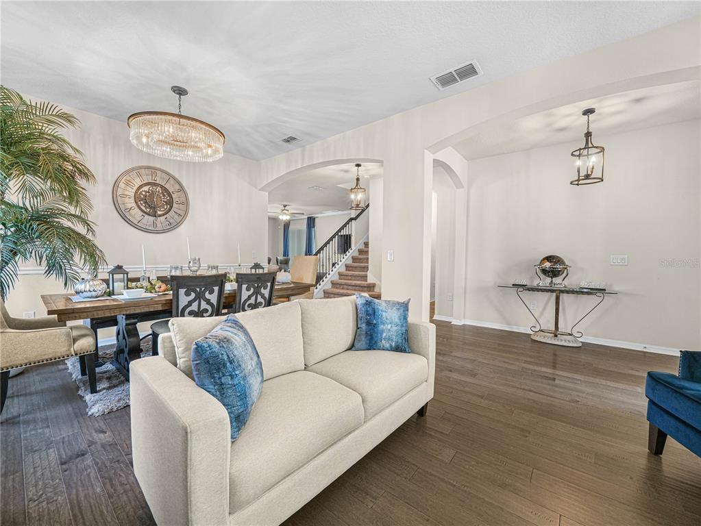 A living and dining area features dark wood floors, blue armchairs, and a white sofa — 184 WHIRLAWAY DRIVE, DAVENPORT, FL