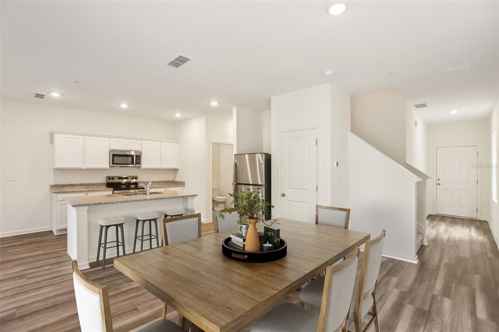 An open-concept kitchen and dining area features white cabinets, stainless appliances, and wood-look flooring — 2570 GREY HAWK DRIVE,, KISSIMMEE, FL