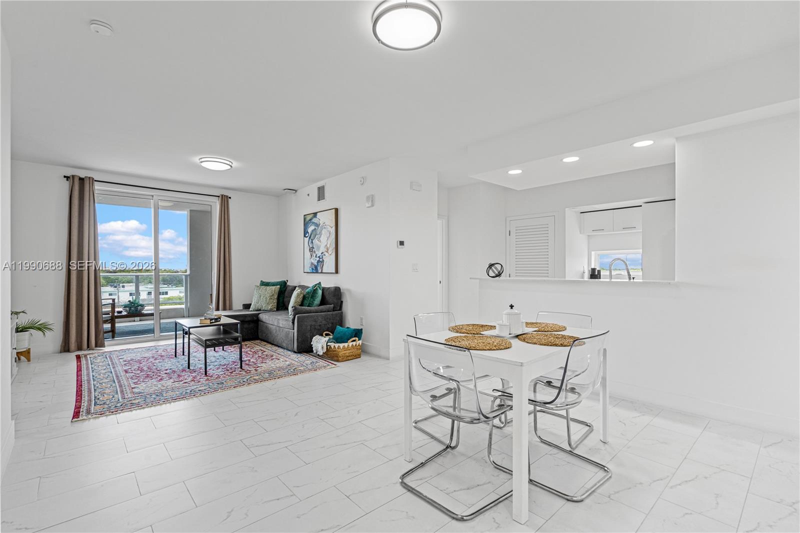 An open-concept living and dining area features white tile floors and a balcony view — 1850 Monroe St # 308, Hollywood FL 33020, HOLLYWOOD, FL