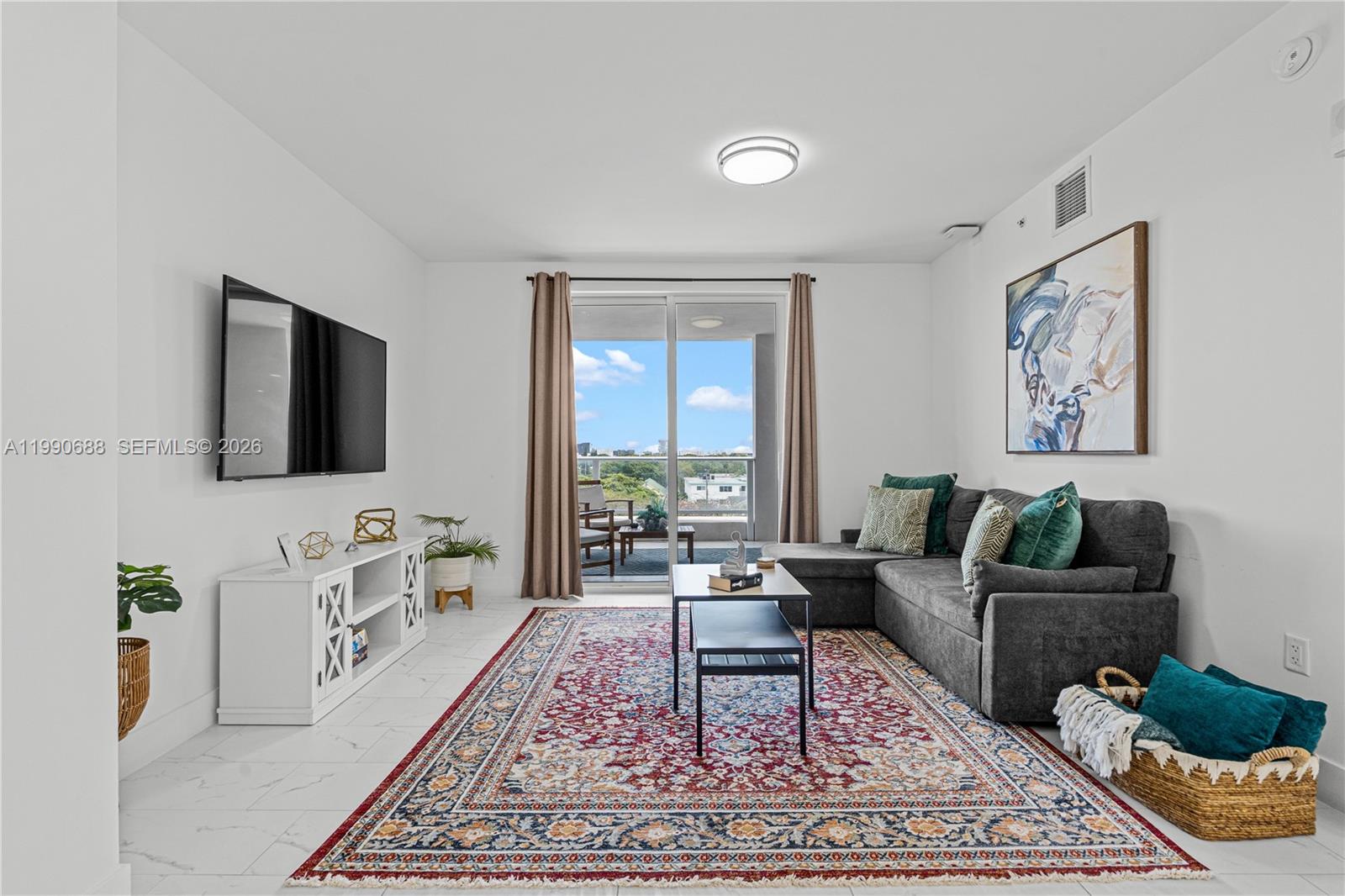 A living room features a grey sectional sofa, a patterned rug, and a balcony view — 1850 Monroe St # 308, Hollywood FL 33020, HOLLYWOOD, FL
