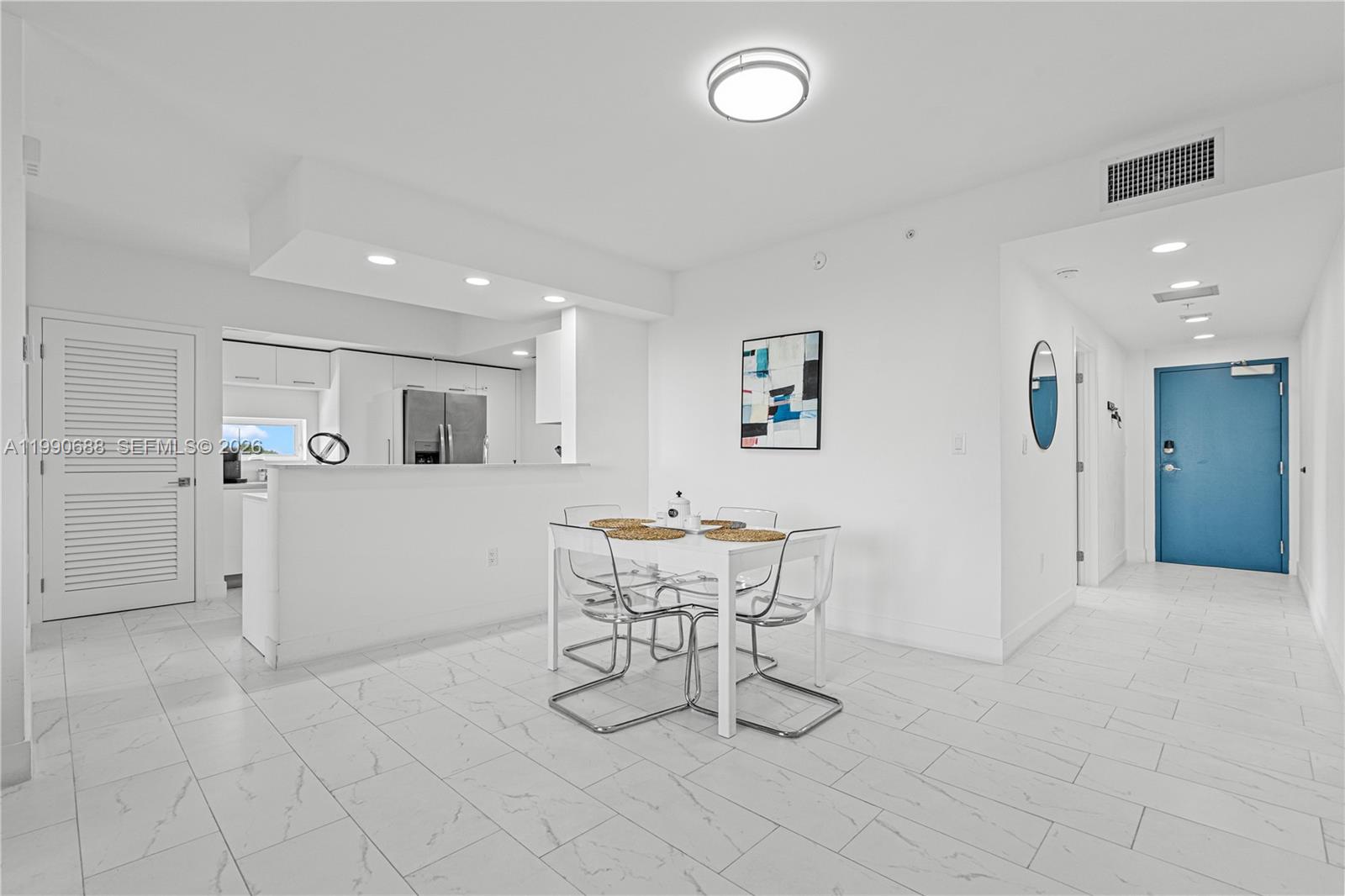 A dining area with a white table and clear chairs sits before an open kitchen — 1850 Monroe St # 308, Hollywood FL 33020, HOLLYWOOD, FL