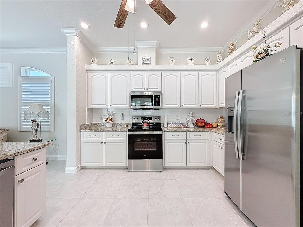A kitchen features white cabinets, stainless steel appliances, granite countertops, and light-colored tile flooring — 1321 VALIANT AVENUE, SPRING HILL, FL