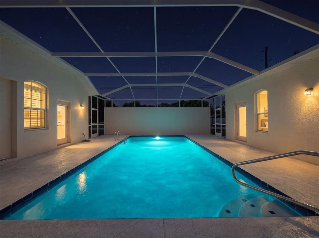 A rectangular swimming pool is enclosed by a screened lanai at night — 1321 VALIANT AVENUE, SPRING HILL, FL