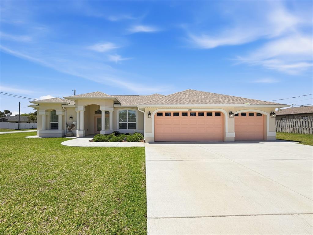 A single-story house with a beige exterior, a three-car garage, and a concrete driveway — 1321 VALIANT AVENUE, SPRING HILL, FL