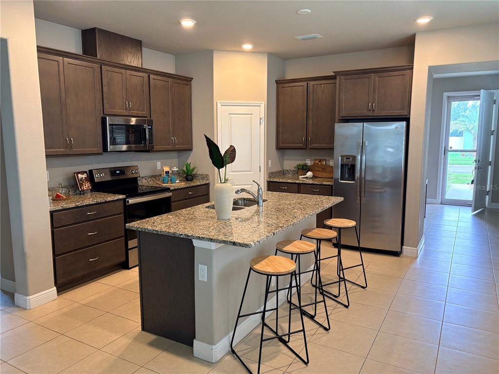 A kitchen features dark wood cabinets, granite countertops, a center island, and stainless steel appliances — 14543 STRATHGLASS DRIVE, HUDSON, FL