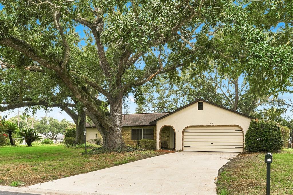 A single-story house with a beige exterior, a two-car garage, and a large oak tree — 512 PONDEROSA DRIVE, ST CLOUD, FL