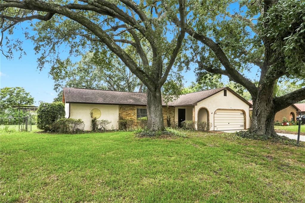 A single-story house with a brick and stucco exterior sits behind large oak trees — 512 PONDEROSA DRIVE, ST CLOUD, FL