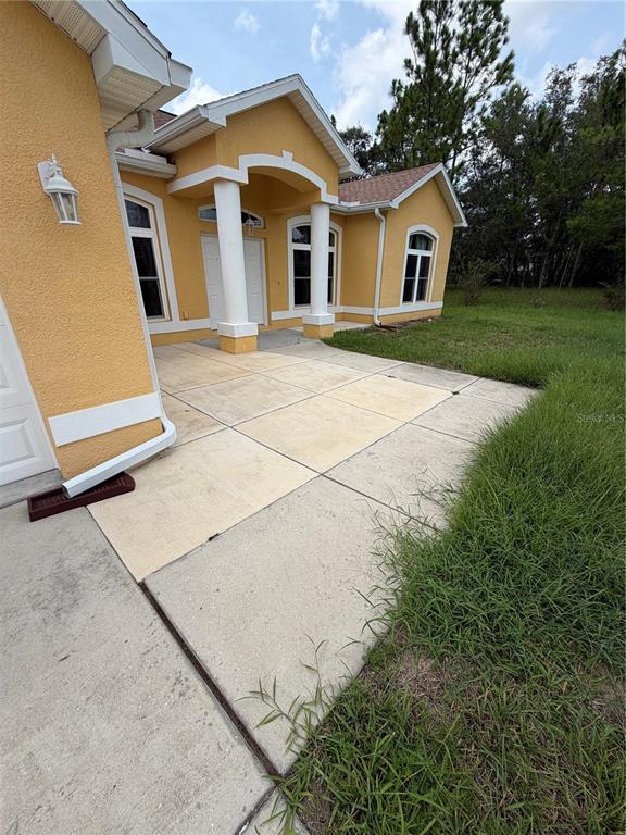 A yellow stucco house exterior features a concrete walkway leading to a covered front entrance — 18179 MABERLY  ROAD, WEEKI WACHEE, FL