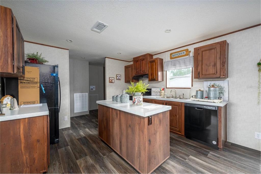 A kitchen features wood cabinets, a central island, black appliances, and wood-look flooring — 1065 NE COUNTY ROAD 125, LAWTEY, FL