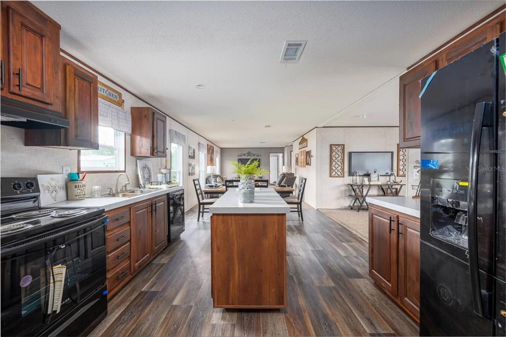 A kitchen with wood cabinets, a central island, and black appliances opens into a living area — 1065 NE COUNTY ROAD 125, LAWTEY, FL