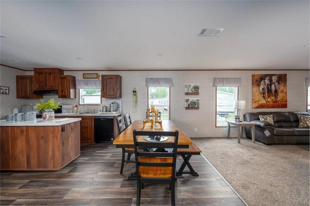An open-concept kitchen, dining area, and living room featuring wood-look flooring and carpeted floors — 1065 NE COUNTY ROAD 125, LAWTEY, FL