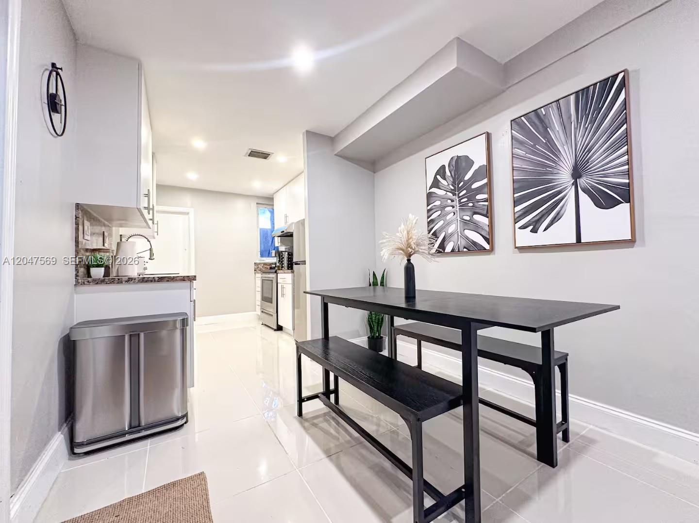 A dining area with a black table and benches sits adjacent to a white kitchen — 174 NE 55th St # 1, Miami FL 33137, MIAMI, FL