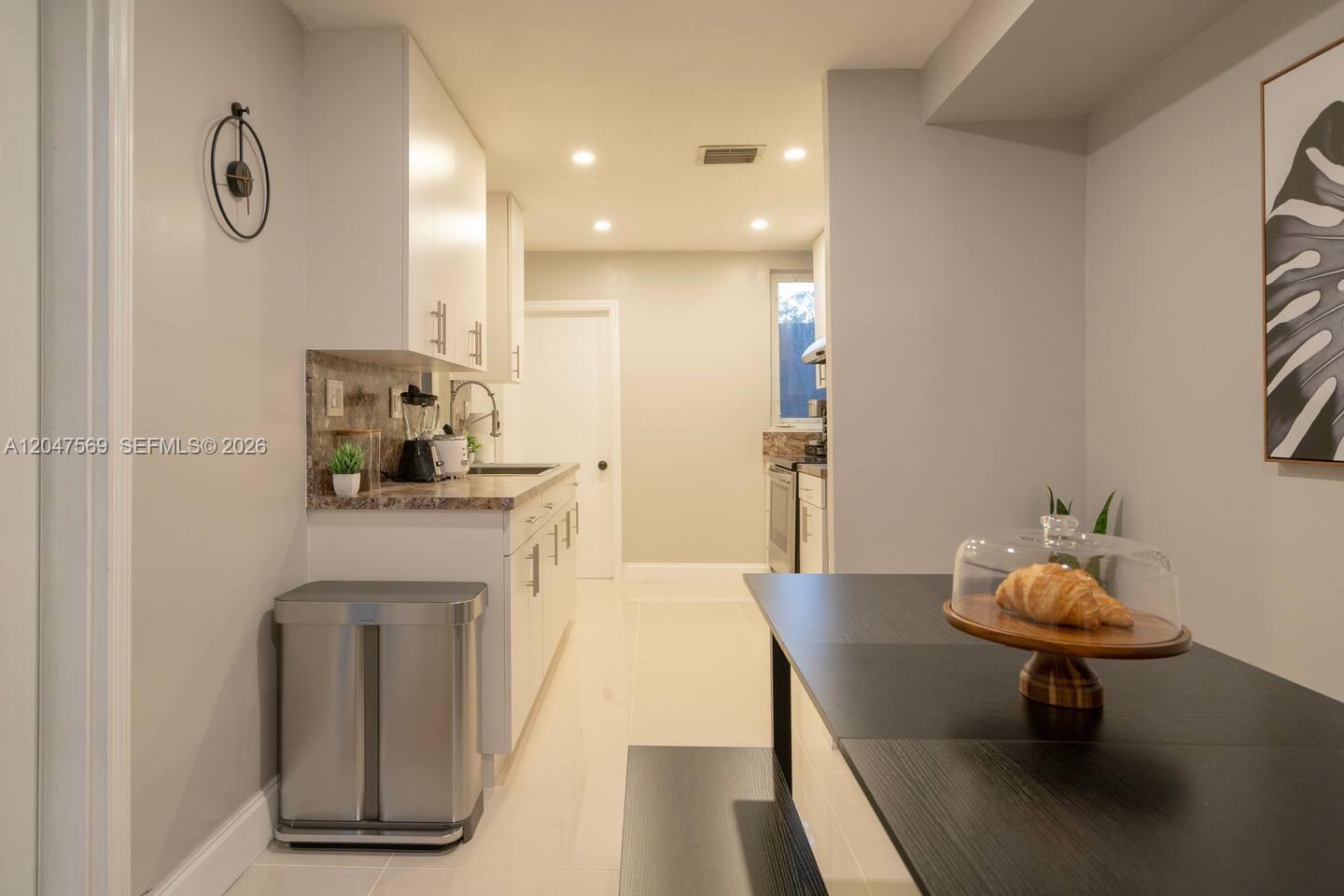 A kitchen features white cabinetry, light countertops, a stainless steel trash can, and a table — 174 NE 55th St # 1, Miami FL 33137, MIAMI, FL