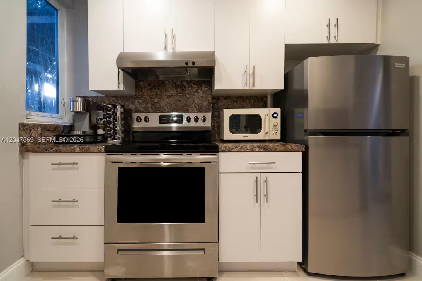 A kitchen features white cabinets, stainless steel appliances, and a dark granite countertop — 174 NE 55th St # 1, Miami FL 33137, MIAMI, FL