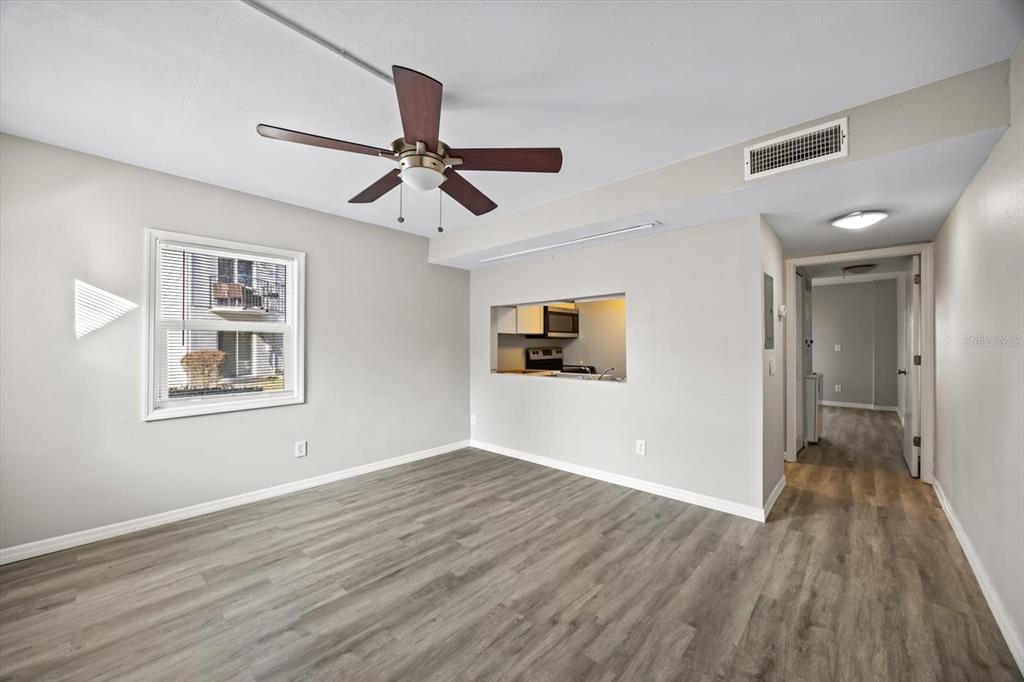 An empty living room with wood-look flooring, a ceiling fan, and a kitchen pass-through window — 7169 E BANK DRIVE UNIT 7169, TAMPA, FL