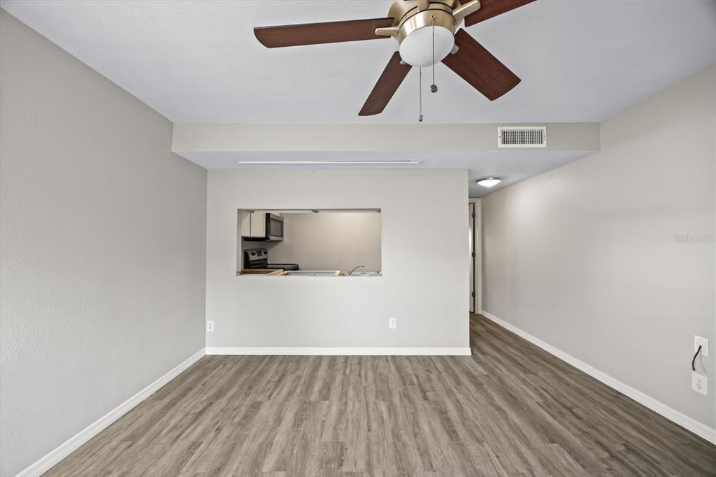 A living room with light gray walls, wood-look flooring, a ceiling fan, and a pass-through window — 7169 E BANK DRIVE UNIT 7169, TAMPA, FL