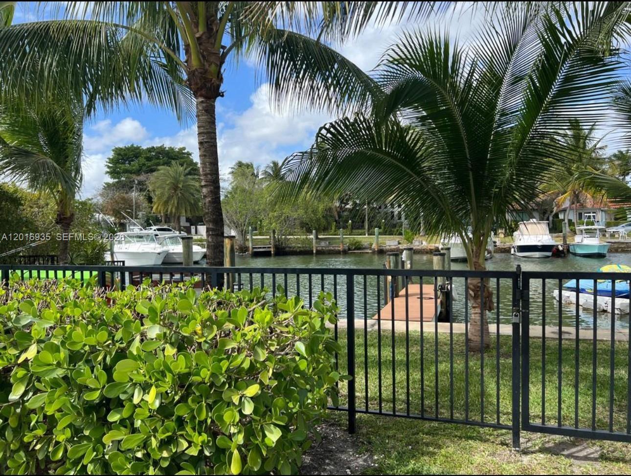 A view of a canal with docked boats and palm trees behind a black metal fence — 1082 NE 89th St, Miami FL 33138, MIAMI, FL