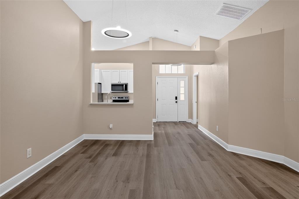 An interior view shows a dining area with wood-look flooring, vaulted ceilings, and a kitchen pass-through — 12421 EARLY RUN LANE, RIVERVIEW, FL