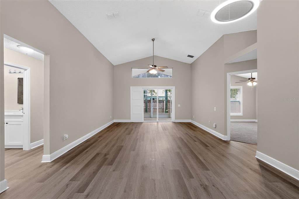 A living room with vaulted ceilings, wood-look flooring, a ceiling fan, and sliding glass doors — 12421 EARLY RUN LANE, RIVERVIEW, FL