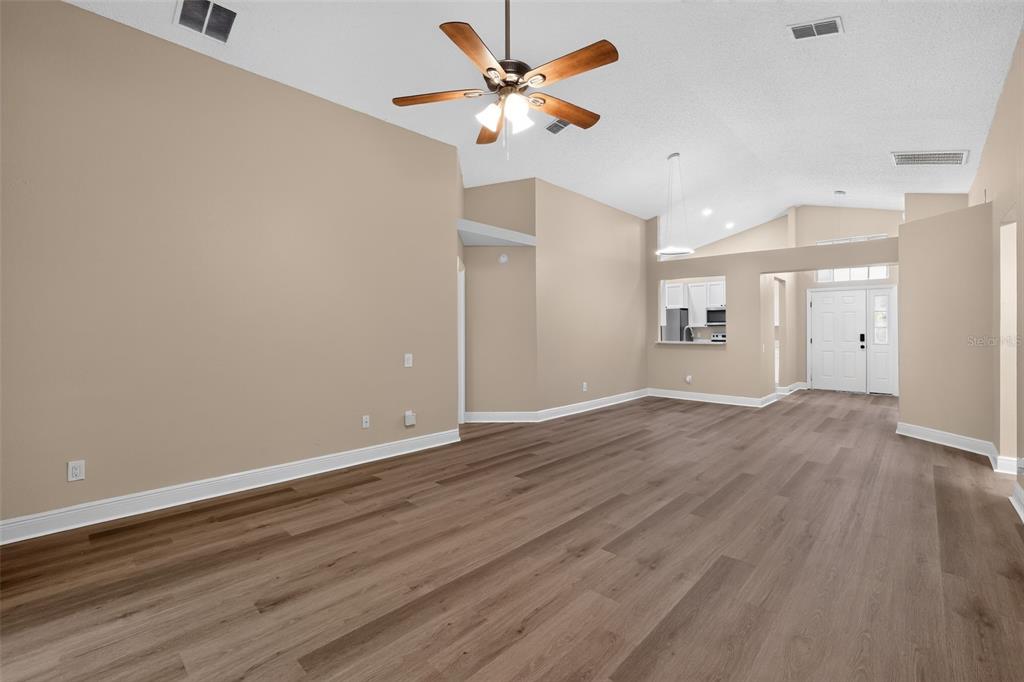 An open-concept living room features light beige walls, wood-look flooring, and a vaulted ceiling — 12421 EARLY RUN LANE, RIVERVIEW, FL