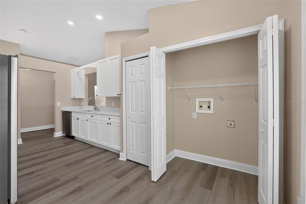 A laundry closet with hookups sits next to a kitchen featuring white cabinets and flooring — 12421 EARLY RUN LANE, RIVERVIEW, FL