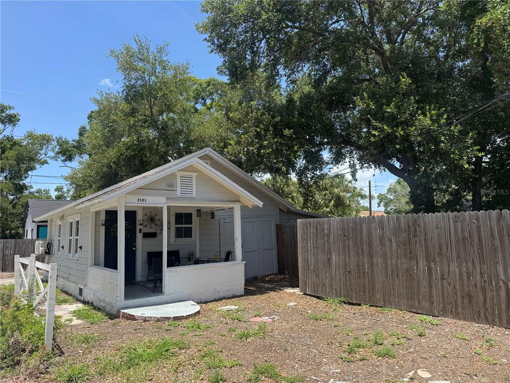 A small, light-colored house with a front porch sits behind a wooden fence — 2521 4TH STREET S, ST PETERSBURG, FL