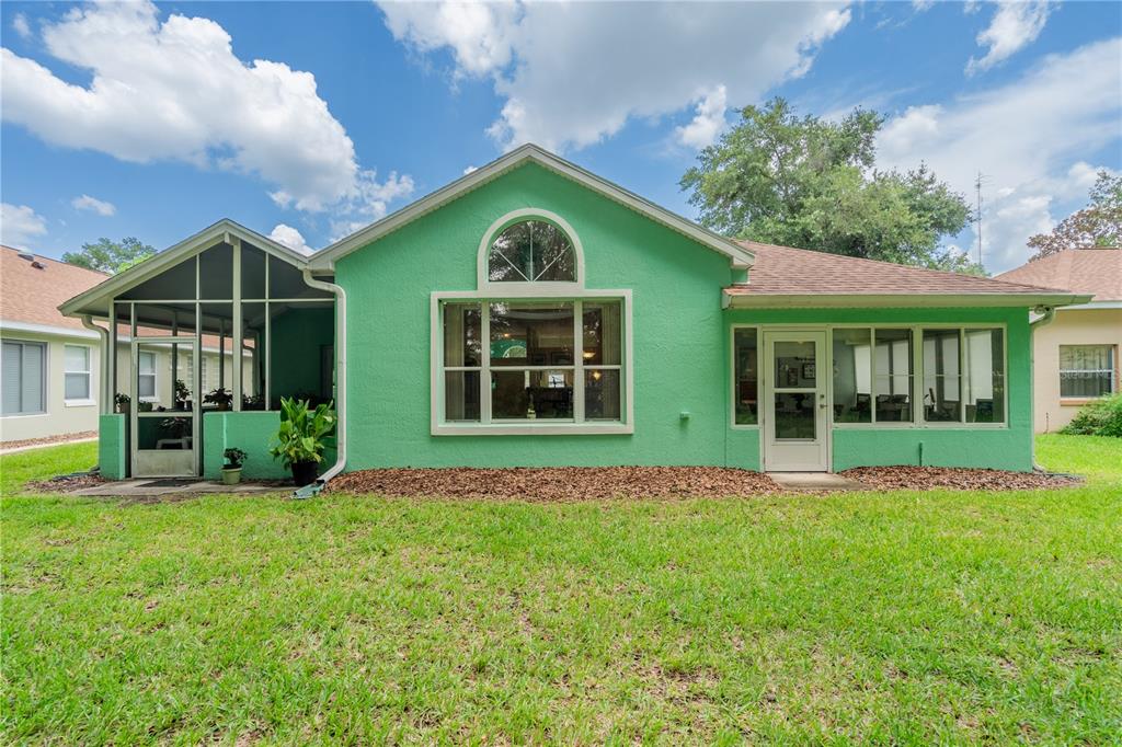 The exterior of a bright green house features a screened-in porch and a large window — 10971 SW 69TH CIRCLE, OCALA, FL