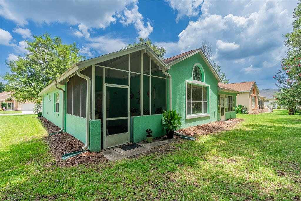 A green stucco house features a screened-in porch and a large arched window — 10971 SW 69TH CIRCLE, OCALA, FL