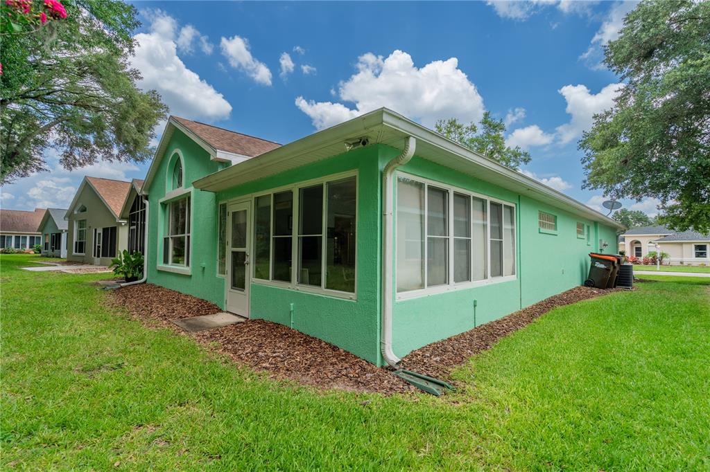 The exterior of a bright green house features a screened-in porch and a white door — 10971 SW 69TH CIRCLE, OCALA, FL