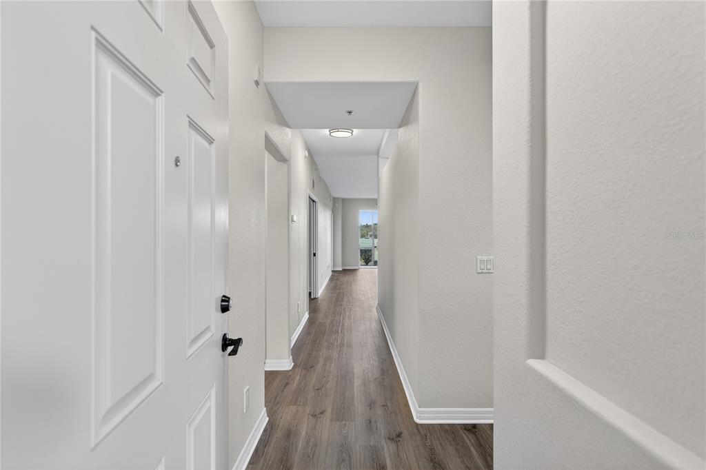 A view from an entryway looking down a hallway with wood-look flooring toward a window — 915 FAIRWAYCOVE LANE UNIT 101, BRADENTON, FL