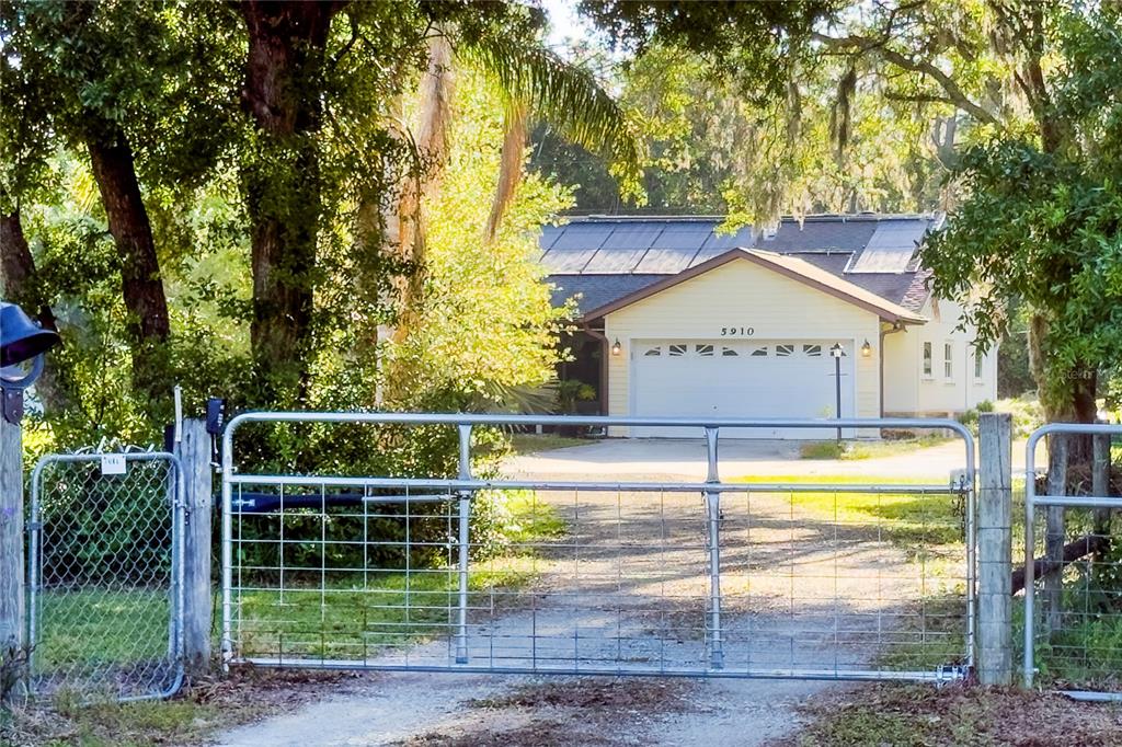 A metal gate stands at the entrance of a driveway leading to a yellow house — 5910 BELLA ROAD, PARRISH, FL